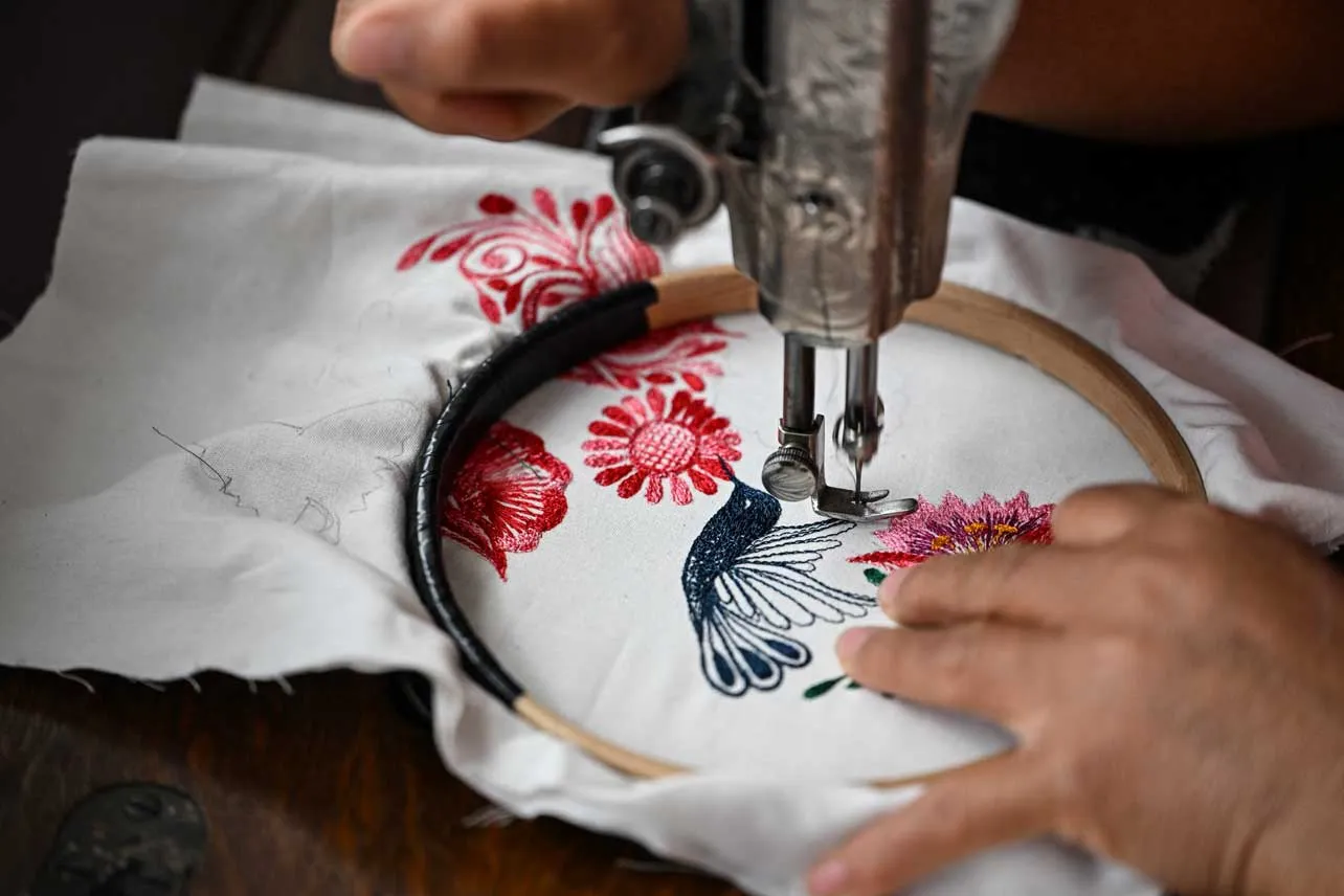Una artista indígena borda un colibrí en una tela blanca.