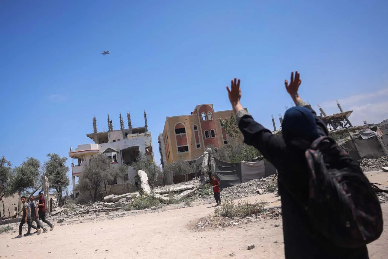 Un persona alza sus brazos mientras en el cielo cruza un avión que reparte ayuda humanitaria en Gaza.