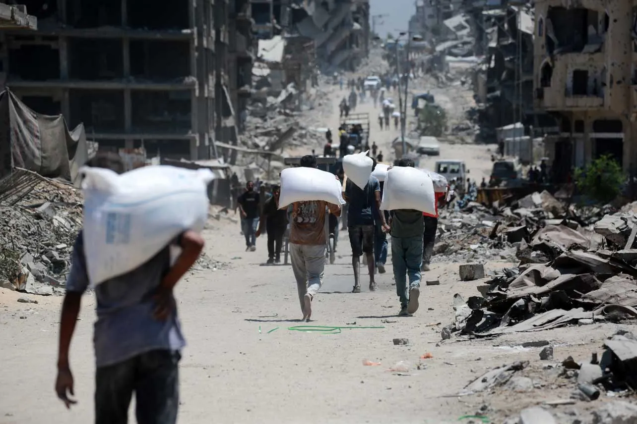 Personas cargando sacos de alimentos entre las ruinas en Gaza.