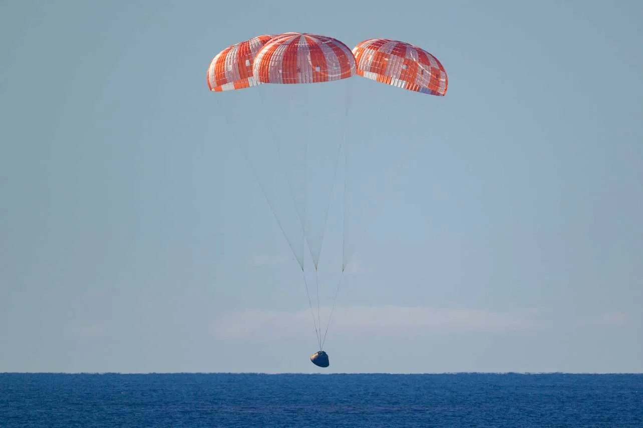 Cápsula del Artemis II cayendo con paracaídas al mar.