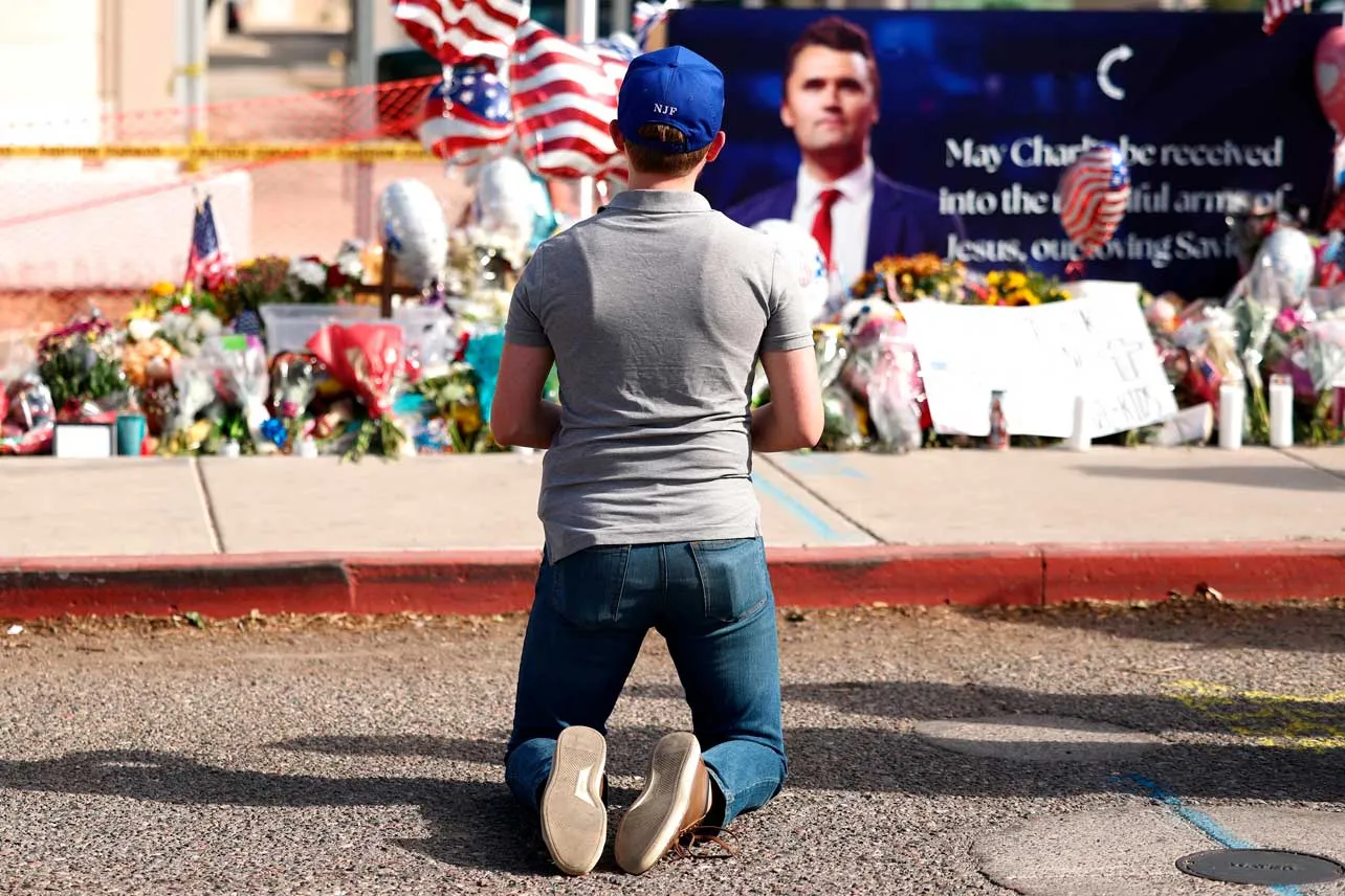 Un persona arrodillada frente a ofrendas tras la muerte de Charlie Kirk.